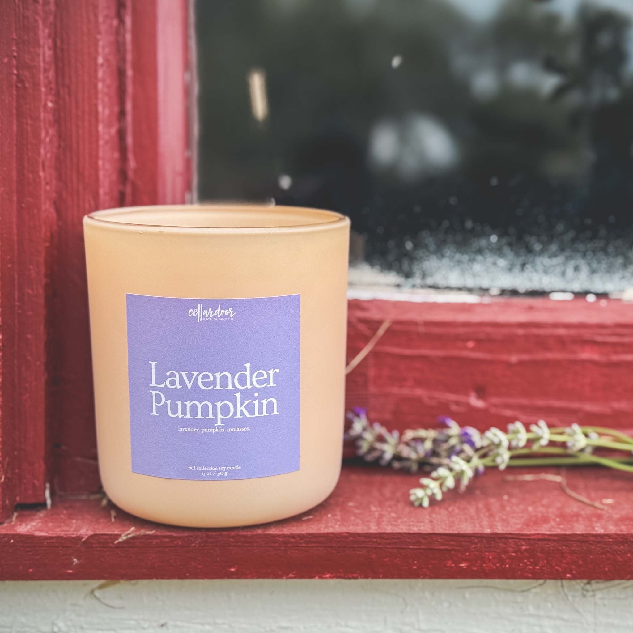 Candle labeled 'Lavender Pumpkin' on a red surface with blurred background