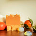 Bar of unlabelled soap named Mandarin Opalite surrounded by mandarin oranges and opalite stones on a wooden surface.