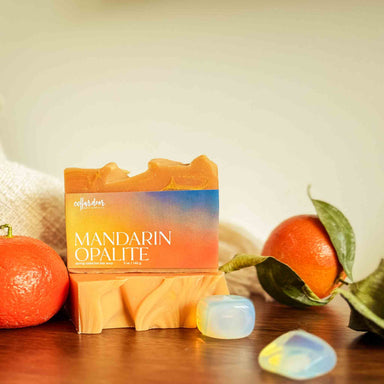 Bar of soap named Mandarin Opalite surrounded by mandarin oranges and opalite stones on a wooden surface.