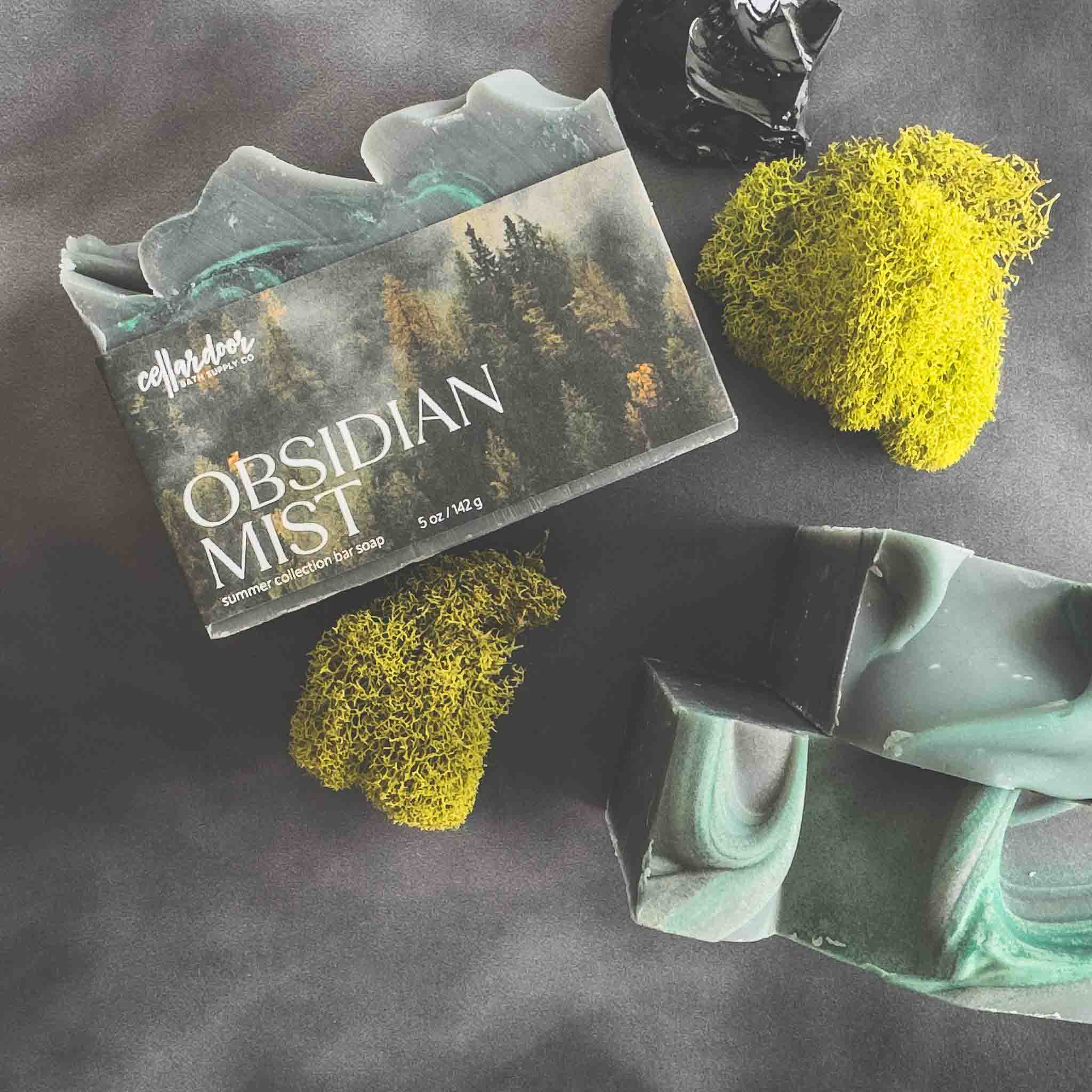 Obsidian Mist soap bar with packaging on a dark surface with moss-like decorations